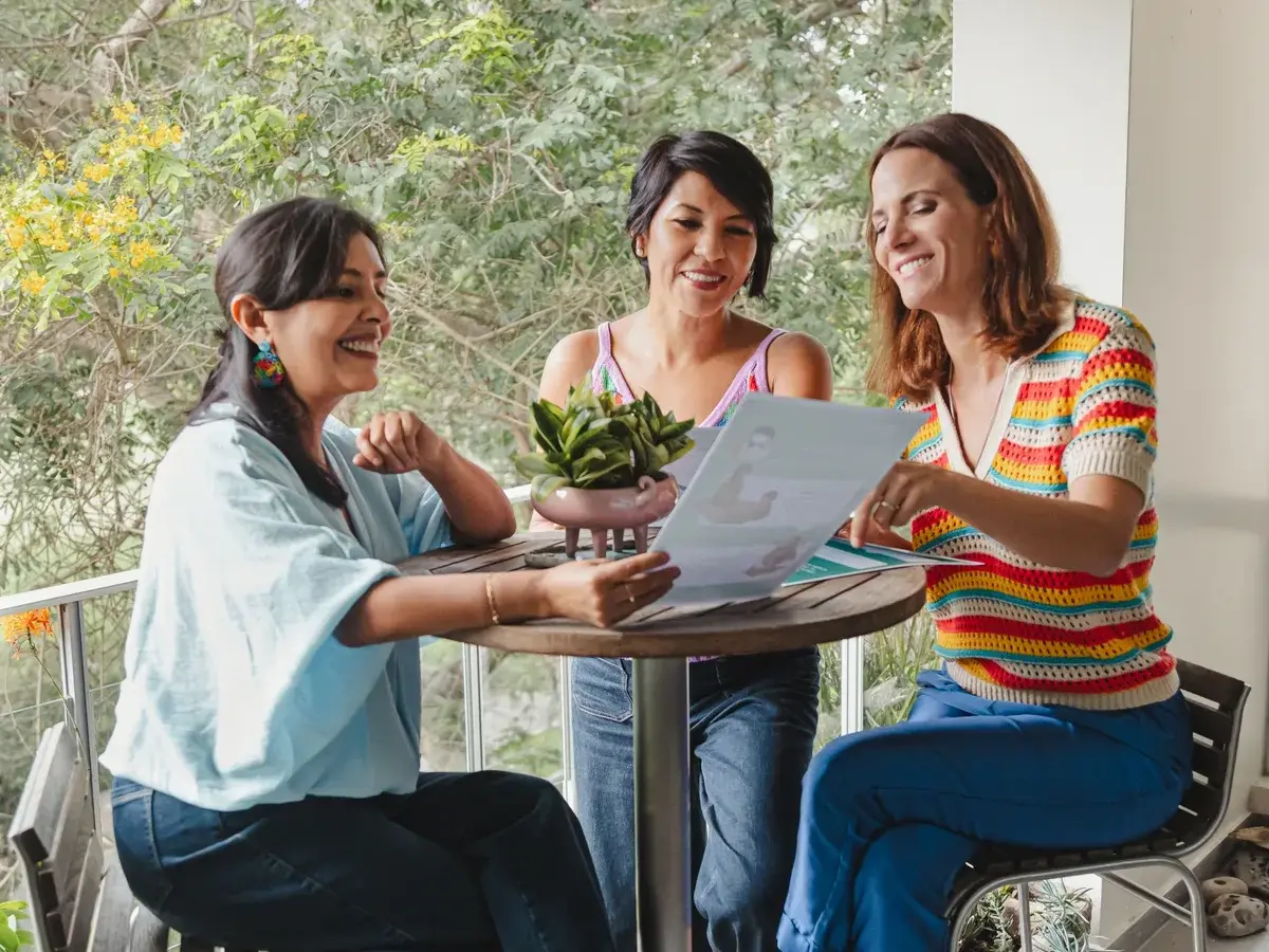 Tres maestras sonriendo mientras revisan materiales pedagógicos